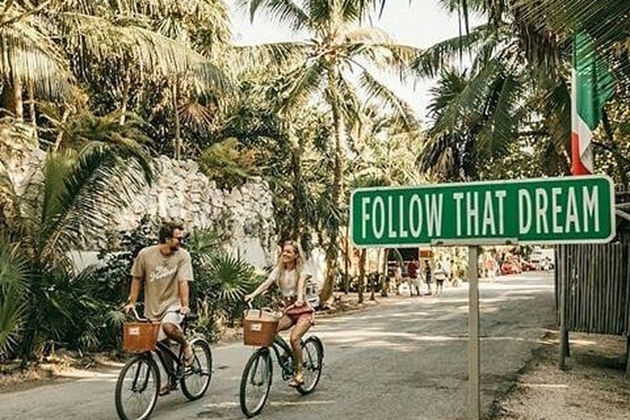 Couple biking down a palm-lined Tulum street